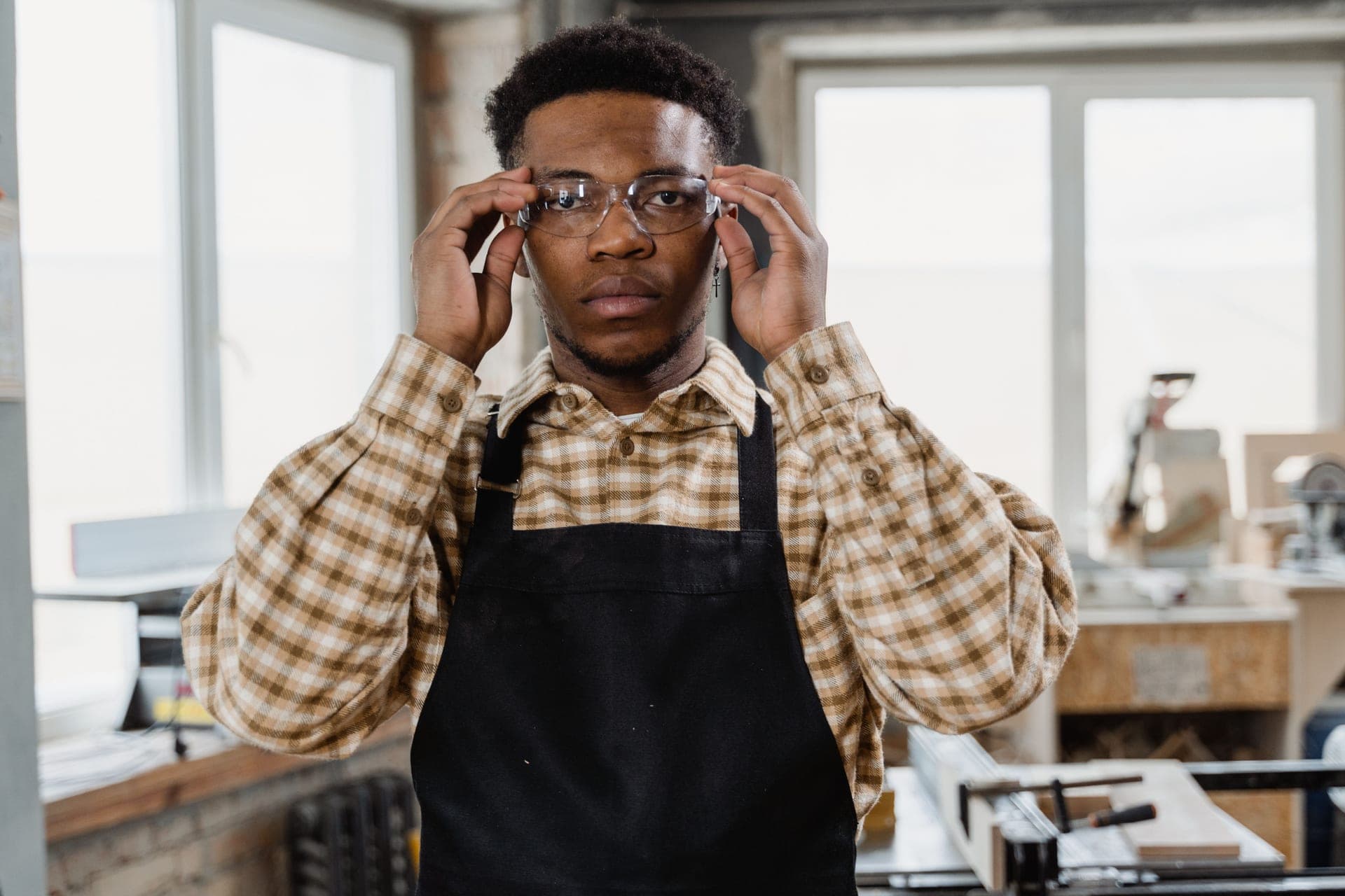 A woodworker in an apron and safety glasses at a workshop bench