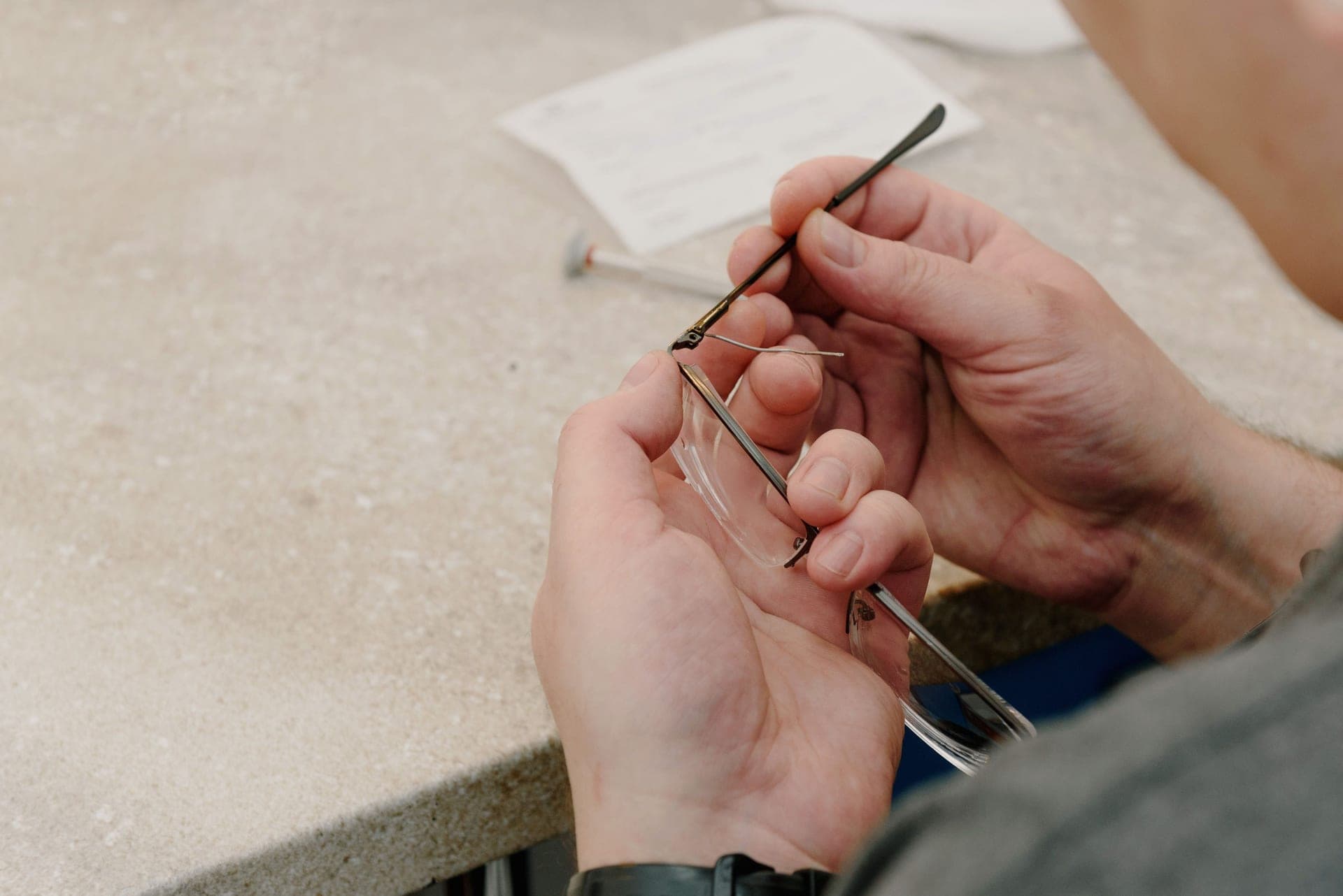 An eyeglass technician tightening the temple screw on a pair of glasses